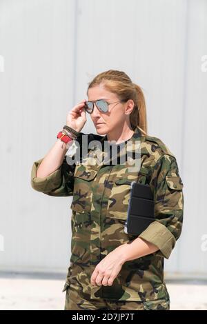 Selbstbewusst reife blonde weibliche Armee Soldat trägt Sonnenbrille bei Militär Basis an sonnigen Tag Stockfoto