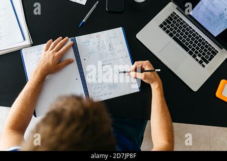 Männliche Schüler lösen mathematische Gleichungen im Arbeitsbuch während der Sitzung Tabelle Stockfoto