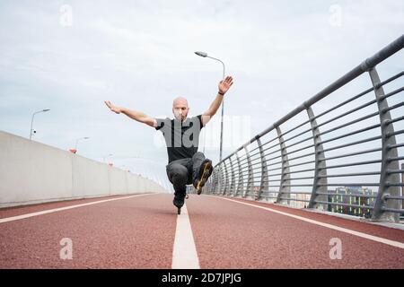 Junger Mann, der Stunt beim Inline-Skaten auf der Brücke gegen Himmel Stockfoto