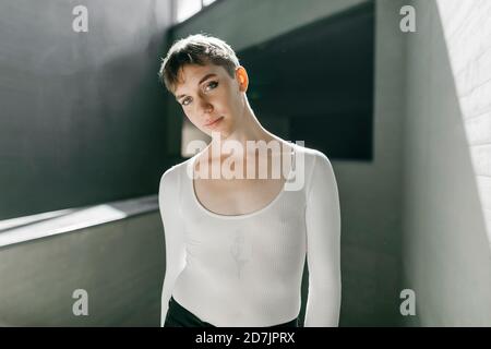 Trans junger Mann in weißem Trikot im Keller stehend Stockfoto