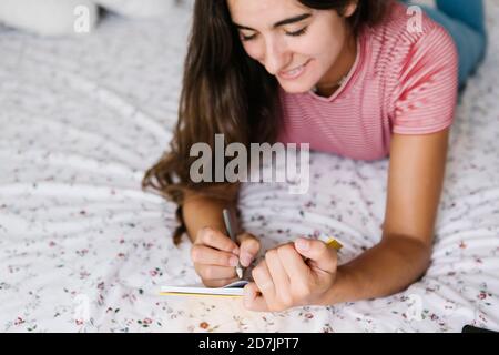 Junge Frau, die sich im Buch Notizen gemacht hat, während sie sich darauf legt Bett zu Hause Stockfoto