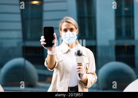 Journalistin trägt Maske zeigt Smartphone, während im Stehen Stadt Stockfoto