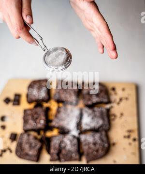 Vertikale Aufnahme eines Bäckers, der eine frisch gebackene Brownies entstaubt Mit Puderzucker Stockfoto