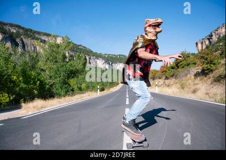 Mann trägt Dinosaurier Maske Skateboarding auf der Straße gegen klaren Himmel Stockfoto