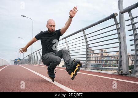 Junger Mann Inline-Skating beim Crouching auf Brücke gegen Himmel Stockfoto