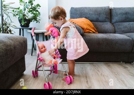 Nettes Baby Mädchen setzen Spielzeug in Baby Kinderwagen beim Stehen Zu Hause Stockfoto