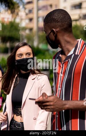 Junges Paar mit Gesichtsmasken während des Spazierens in der Stadt während COVID-19-Ausbruch Stockfoto