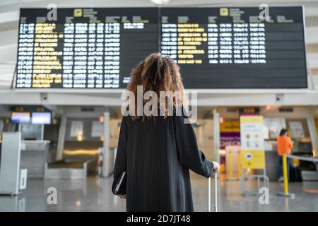 Junge Frau überprüft den Zeitpunkt der Ankunft des Fluges an Bord stehend Am Flughafen Stockfoto