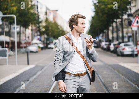 Lächelnder Geschäftsmann, der mit dem Handy telefoniert, während er in der Straßenbahn läuft In der Stadt Stockfoto