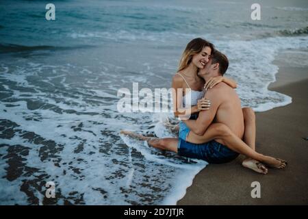 Paar umarmt sich gegenseitig, während sie am Ufer sitzen Strand Stockfoto