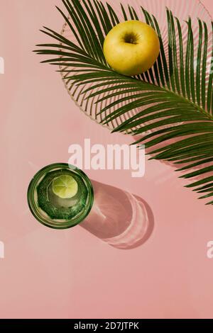 Studioaufnahme von Palmblättern, Glasschale, Glas kohlensäurehaltiges Wasser und einem einzelnen Apfel Stockfoto