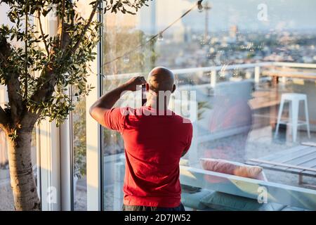 Ein reifer Mann fotografiert den Sonnenuntergang durch das Fenster auf dem Dach Stockfoto