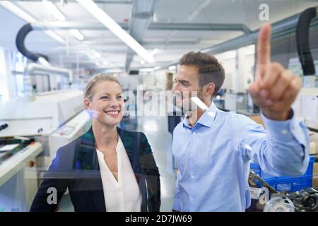 Junger männlicher Techniker zeigt auf grafische Oberfläche auf Glas in Werk Stockfoto