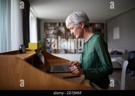 Aktive ältere Frau, die sich während der Arbeit am Laptop konzentriert Stockfoto