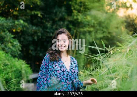 Lächelnd schöne Frau, die inmitten von Pflanzen im Park steht Stockfoto