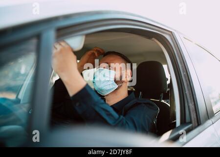 Ein hübscher junger kaukasischer Geschäftsmann in einem schwarzen Hemd mit Gesichtsmaske, der seine Haare aufsetzt und in den Rückspiegel schaut und zur Arbeit geht. Stockfoto