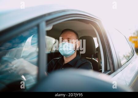 Ein Porträt eines hübschen kaukasischen Geschäftsmannes in einem schwarzen Hemd mit Gesichtsmaske, der ein Auto fährt und zur Arbeit geht. Prävention während der COVID - 19 Stockfoto