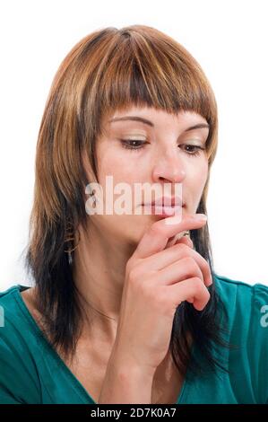 Kopf- und Schulteransicht einer jungen, nachdenklichen Frau mit braunen Haaren und verbeugten Augen, die ihren rechten Zeigefinger an ihr Kinn hält. Stockfoto