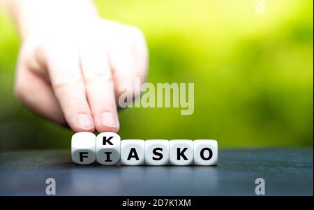 Hand dreht Würfel und ändert den deutschen Ausdruck 'Fiasko' (Fiasco) in 'Kasko' (Deckung). Stockfoto