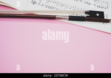 Nahaufnahme eines Geigenbogens mit Noten auf dem Rosa Oberfläche Stockfoto