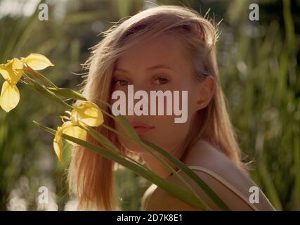 Nahaufnahme einer blonden Frau mit einer Lilie auf einem Sumpf bei Sonnenuntergang. Stockfoto