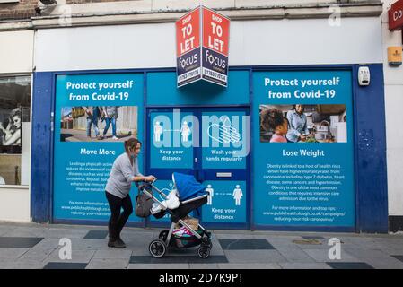 Slough, Großbritannien. Oktober 2020. Eine Frau mit einem Kinderwagen geht vor dem Slough Borough Council COVID-19 öffentliche Informationsauslagen. Die Regierung hat angekündigt, dass Slough seinen COVID-Alarmstatus von Stufe 1 mittlere Warnung auf Stufe 2 hohe Warnung mit Wirkung von 00:01 Uhr am Samstag, dem 24. Oktober ändern wird, nachdem die COVID-19-Fälle anstiegen, was zu einer Infektionsrate von 153 Fällen pro 100,000 führt. Kredit: Mark Kerrison/Alamy Live Nachrichten Stockfoto