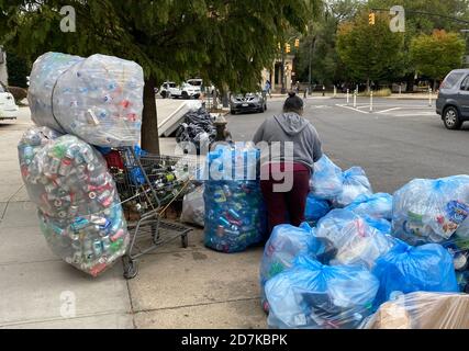 Hart arbeitende Frau sammelt Dosen und Flaschen, die sie aus Mülltüten holt, die von der Sanitärabteilung in Brooklyn, New York, zur Abholung bereitgestellt werden. Stockfoto