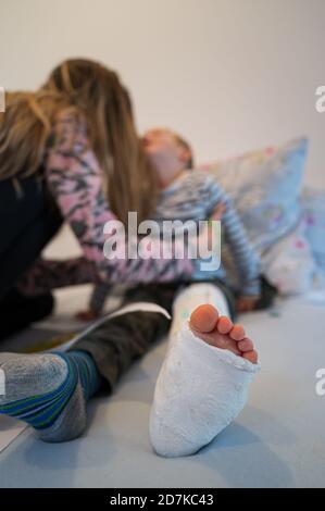 Mutter legte ihr Kleinkind mit einem gebrochenen verletzten Bein in einen Wurf auf sein Bett. Stockfoto