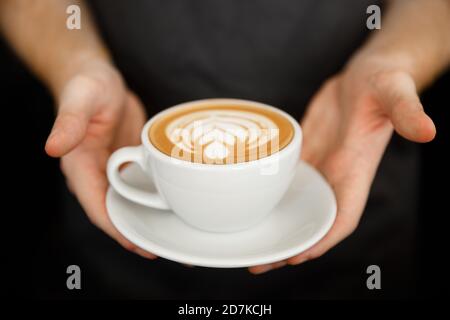 Coffee Business Concept – Nahaufnahme einer Frau, die Kaffee mit Latte-Kunst serviert, während sie im Café steht. Konzentrieren Sie sich auf weibliche Hände, die eine Tasse platzieren Stockfoto