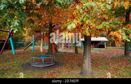 Kinderspielplatz in leuchtenden Farben. Die Laubbäume haben ihre Blätter fallen gelassen. Das sind amerikanische Eichen. Es ist Herbst Stockfoto