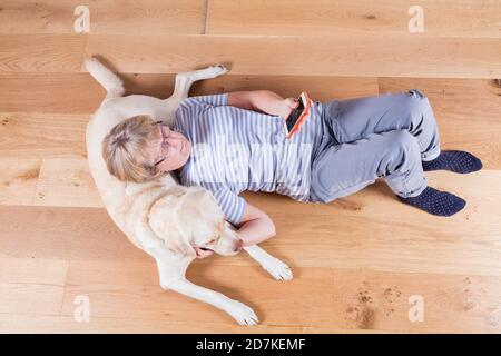 Lady in den späten 60ern, mit ihrem Goldenen Labrador, der mit ihrem Smartphone auf dem Boden liegt. Stockfoto