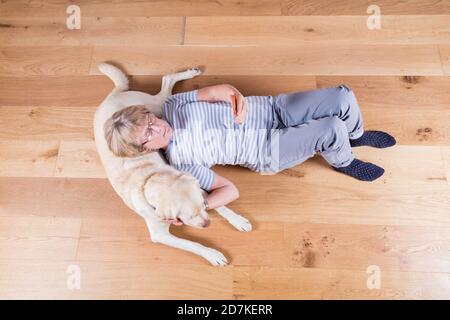 Lady in den späten 60ern, mit ihrem Goldenen Labrador, der mit ihrem Smartphone auf dem Boden liegt. Stockfoto