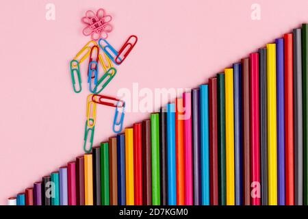 Mann aus mehrfarbigen Büroklammern geht die Treppe hinauf Mehrfarbige Stifte isoliert Stockfoto