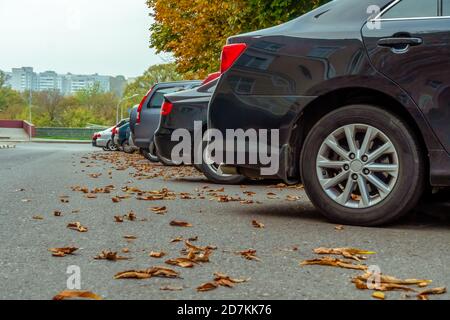Hintere Stoßstangen von Autos auf dem Parkplatz mit herbstlichen Blättern. Foto von der Seite. Parkplatz Stockfoto