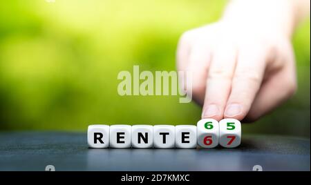 Hand dreht Würfel und ändert den deutschen Ausdruck "Rente 67" (Ruhestand 67) zu "Rente 65" (Ruhestand 65). Stockfoto