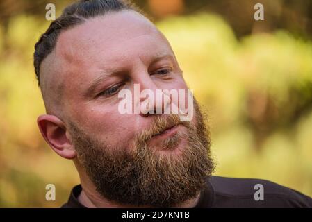 Hipster Stil bärtiger Mann. Der attraktive Mann die Blondine mit langen Haaren des europäischen Auftritts mit einem Bart. Mann in braunem T-Shirt. Mann im Wald Stockfoto
