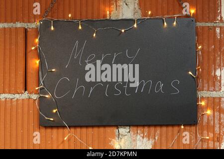 Frohe Weihnachten Inschrift auf der schwarzen Kreidetafel beleuchtet von Girlanden Stockfoto