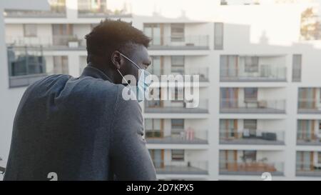 Schwarzer Mann mit medizinischer Maske auf dem Balkon. Quarantäne und psychische Probleme. Hochwertige Fotos Stockfoto