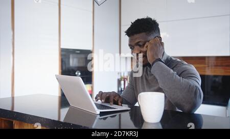 Remote arbeiten. afroamerikanischer schwarzer Geschäftsmann, der in seiner Wohnung telefoniert, während er auf den Laptop schaut. Hochwertige Fotos Stockfoto