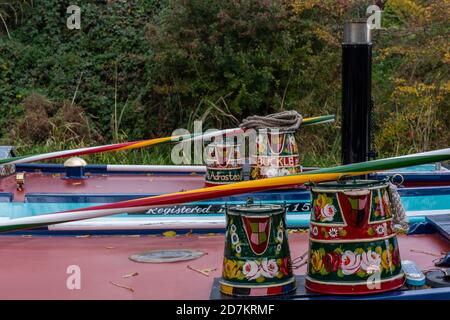 rosen und Burgen im traditionellen Stil auf Eimern und Gießkannen auf der Spitze der schmalen Boote und Lastkähne auf dem Grand Union Kanal gemalt. Stockfoto