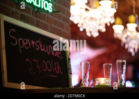 Warendorf, Deutschland. Oktober 2020. Kurz vor der Ausgangssperre stehen drei leere Gläser Bier neben einem Kreideschild mit der Aufschrift "Ausgangssperre 23:00" auf einem Tisch in der Warendorf Bar #One. In Nordrhein-Westfalen wurde eine obligatorische Schließzeit zwischen 11 und 6 Uhr für Restaurants in allen Gemeinden mit hohen Neuinfektionen eingeführt. Die Ausgangssperre gilt in Gemeinden mit 50 oder mehr Neuinfektionen pro 100,000 Einwohner innerhalb von sieben Tagen. Quelle: Guido Kirchner/dpa/Alamy Live News Stockfoto