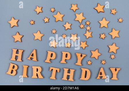 Worte Happy Birthday in Holzbuchstaben geschrieben auf einem grauen Hintergrund. Dekoration mit Holzsternen. Text auf der Tabelle für Design oder Konzept. Stockfoto