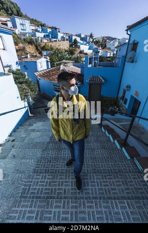 Vertikale Aufnahme eines Mannes, der eine Gesichtsmask und eine trägt Gelbe Jacke und die Treppe im Freien hinauf Stockfoto