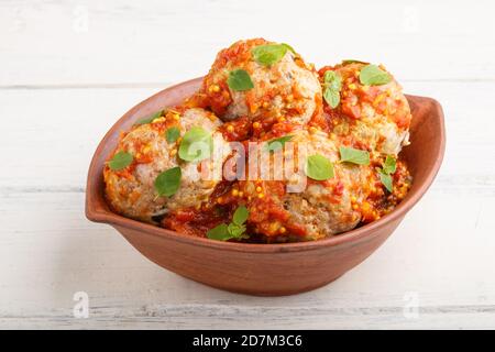 Fleischbällchen aus Schweinefleisch mit Tomatensauce, Oregano-Blättern, Gewürzen und Kräutern in Tonschüssel auf weißem Holzhintergrund. Seitenansicht, Nahaufnahme Stockfoto