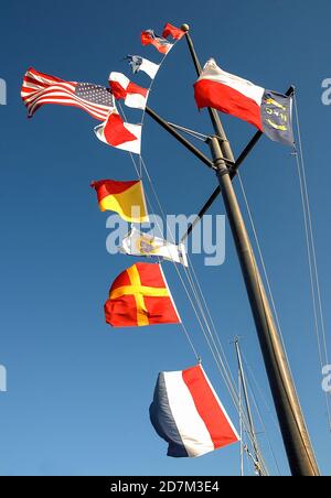 Eine gegen das Licht gedrehte Ansicht der wellenden Flagge auf ihrem schwarzen Mast, Streifen leuchten rot und weiß vor graublauem Himmel, Fort Macon State Park, North Carolina. Stockfoto