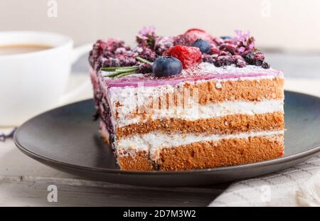 Beerenkuchen mit Milchcreme und Heidelbeermarmelade auf blauer Keramikplatte mit Tasse Kaffee und frischen Heidelbeeren auf weißem Holzhintergrund. Seitenansicht, c Stockfoto