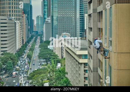 Manila, Philippinen - 02. Feb 2020: Straßen von Makati Stadt während des Tages. Kletterer erklimmen die Wand eines Wolkenkratzers. Stockfoto