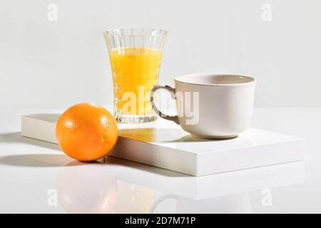 Eine Tasse neben einer ganzen Orange mit einem Glas Von Orangensaft hinter Stockfoto