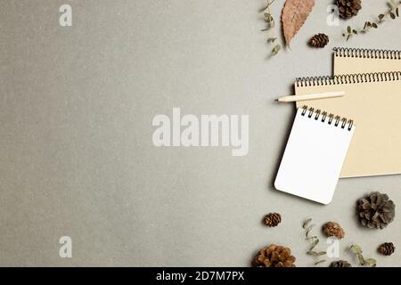 Notizbuch mit trockenen Blättern, Tannenzapfen auf grauem Hintergrund. Flach liegend, Draufsicht, Kopierraum. Arbeits- und Studienort. Herbst- und Winterkonzept Stockfoto