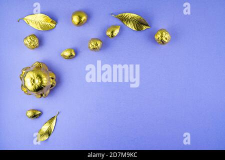 Kürbisse, Nüsse und Blätter in Gold auf violettem Hintergrund gemalt. Flaches Layout mit Platz für Text. Hochwertige Fotos Stockfoto
